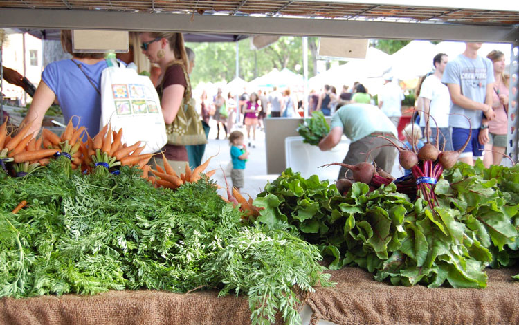 bunches of carrots and beets on a table in front of a bunch of people